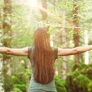 kvinde står meditativt med udstrakte arme i en skov