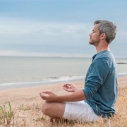 mand sidder i meditationsstilling ved stranden og har lukkede øjne