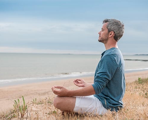 mand sidder i meditationsstilling ved stranden og har lukkede øjne