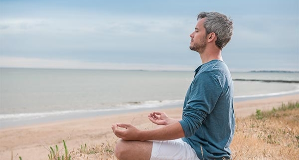 mand sidder i meditationsstilling ved stranden og har lukkede øjne