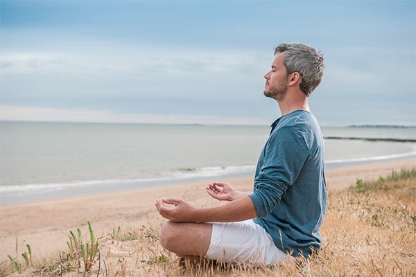 mand sidder i meditationsstilling ved stranden og har lukkede øjne