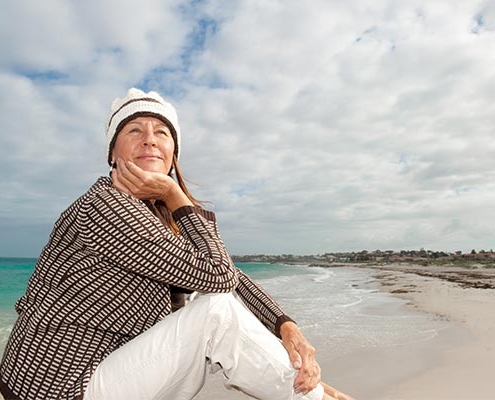 ældre kvinde sidder eftertænksomt i strandkanten