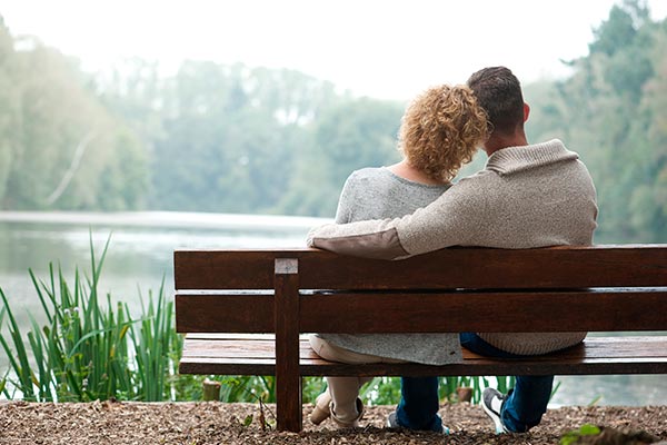 kærestepar sidder tæt sammen på en bænk og kigger udover en sø
